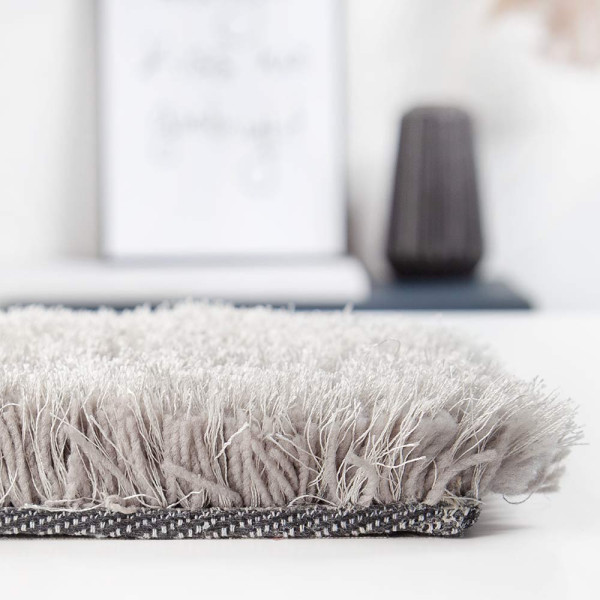 Hochfloriger, kuscheliger Teppich in Hellgrau liegt auf einem glatten Untergrund. Die Teppichkanten sind weich und zeigen ein flauschiges, einheitliches Texturmuster.