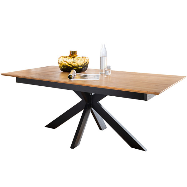 Holztisch mit schwarzem Metallgestell steht in einem Raum. Auf dem Tisch befinden sich eine goldene Vase, eine Wasserflasche und ein Glas, neben einer gerollten Zeitschrift.