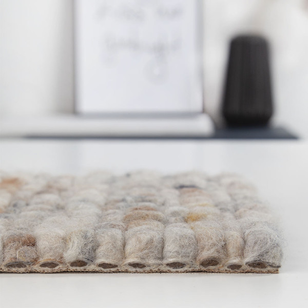 Zarter Webteppich in Beige, bestehend aus Schurwolle. Die strukturierte Oberfläche zeigt kleine, runde Muster und verleiht dem Raum eine gemütliche Atmosphäre. Ideal für nachhaltige Einrichtungsstile.