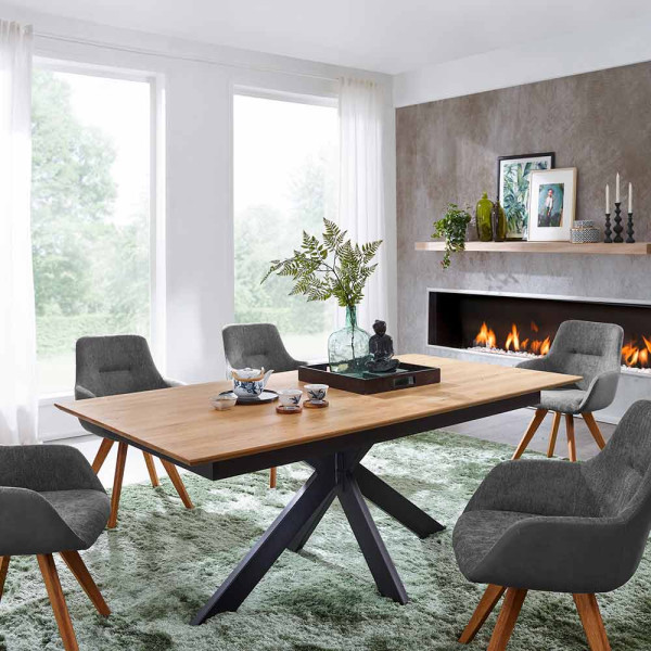 Holztisch mit schwarzem Metallgestell steht in einem Raum. Auf dem Tisch befinden sich eine goldene Vase, eine Wasserflasche und ein Glas, neben einer gerollten Zeitschrift.