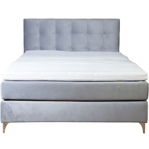 Boxspringbett mit grauem Stoffbezug steht auf einem Boden. Die Matratze hat einen Topper und ist in einer geschlossenen Position. Das Bett hat ein gepolstertes Kopfteil mit quadratischer Steppung.