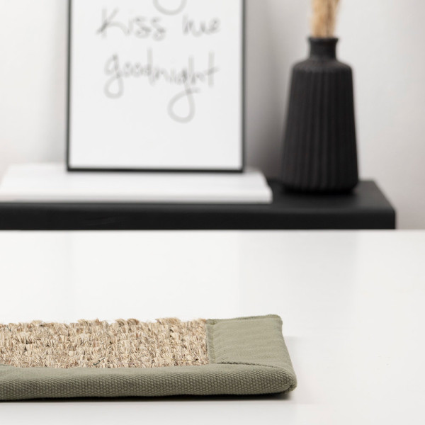 Sisal-Gewebe mit naturfarbenen Fasern ist sorgfältig verarbeitet und zeigt eine strukturierte Oberfläche. Rechts schließt eine graue Stoffkante ab, die die Textur ergänzt.