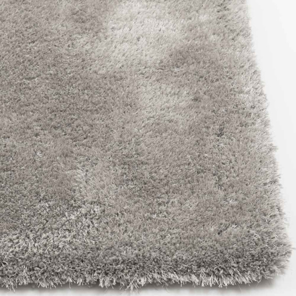 Hochfloriger, kuscheliger Teppich in Hellgrau liegt auf einem glatten Untergrund. Die Teppichkanten sind weich und zeigen ein flauschiges, einheitliches Texturmuster.