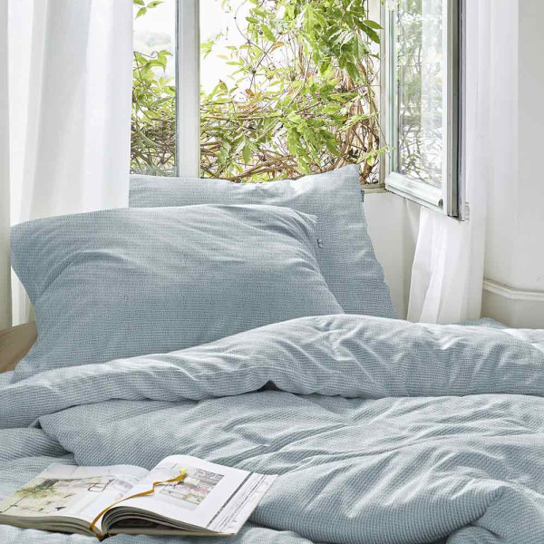 Zart gemusterte Irisette Seersucker-Bettwäsche in Hellblau liegt flach. Kissenbezug und Bettlaken sind ordentlich gefaltet und zeigen die textile Struktur und das dezente Design.