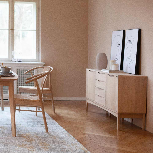 Stylishe Anrichte aus geölter Eiche mit zwei Türen und drei Schubladen steht auf vier schmalen Beinen. Die Oberfläche ist glatt und in einem hellen Holzton gehalten.