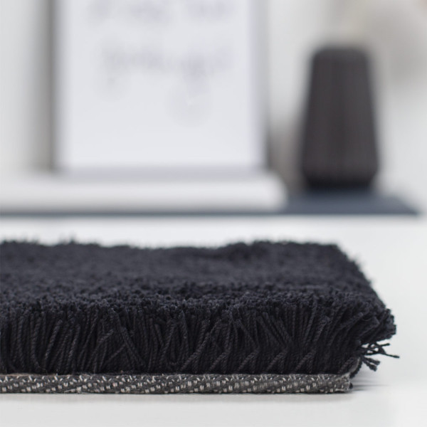 Schwarzer, weicher Webteppich aus Polyester mit fransigen Kanten. Der Teppich eignet sich für individuelle Maßanfertigungen und bietet eine vielseitige Gestaltungsmöglichkeit für verschiedene Räumlichkeiten.