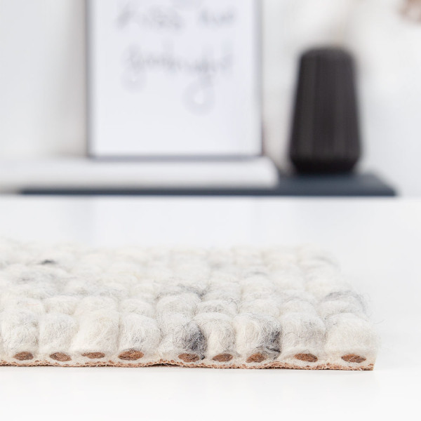 Heller, nachhaltiger Webteppich aus Schurwolle mit einer strukturierten, gepunkteten Oberfläche in Weiß und Grau. Der Teppich eignet sich zur individuellen Gestaltung nach Maß.