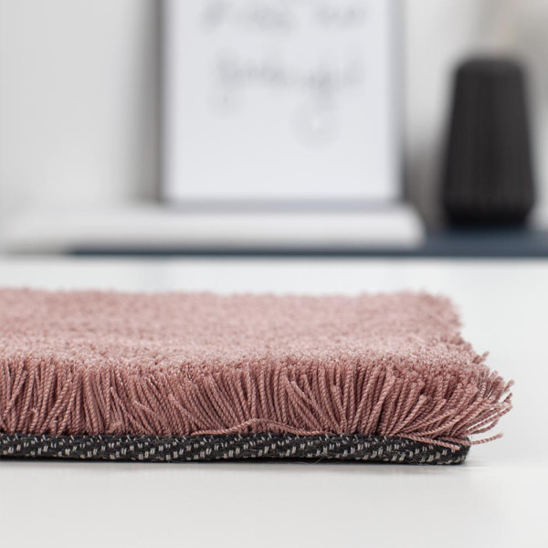 Weicher, rosafarbener Teppich aus Polyester liegt auf einem hellen Untergrund. Die Oberfläche ist kurzflorig und einladend. Der Teppich eignet sich für individuelle Gestaltung in verschiedenen Größen.