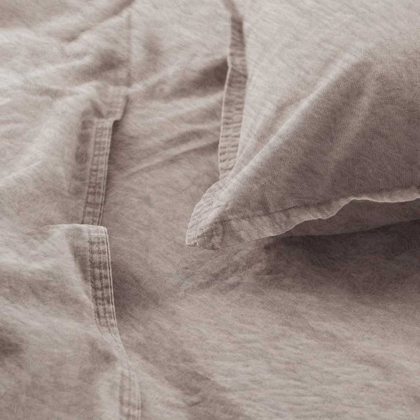 Flanell-Bettwäsche in sanfter, beiger Farbe liegt drapiert auf einem Bett. Ein Kissenbezug und die Bettdecke sind sichtbar, zusammen mit einem Detailansicht-Ausschnitt der Naht.