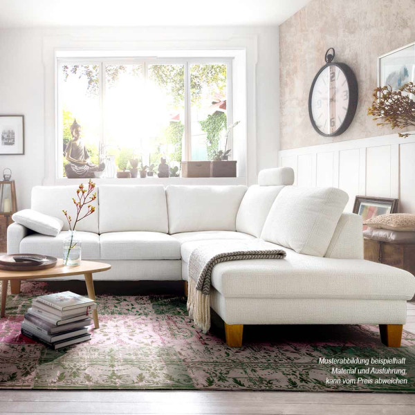 Helle, moderne Couchgarnitur in L-Form steht im Wohnzimmer. Eine runde Tischplatte mit Blumen und Büchern ergänzt die Einrichtung. Große Fenster bieten Ausblick auf den Garten.