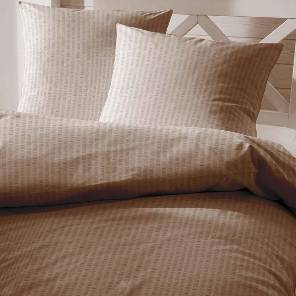 Weiche Bettwäsche in Taupe im Soft Seersucker-Stil liegt auf einem Bett. Der Kissenbezug ist ebenfalls in Taupe und zeigt eine leichte Struktur.