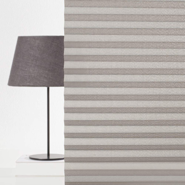 Graues, halbtransparentes Plissee mit mehreren Falten. Es wird für Sicht- und Sonnenschutz genutzt und bietet eine elegante, funktionale Gestaltungsmöglichkeit für Fenster.
