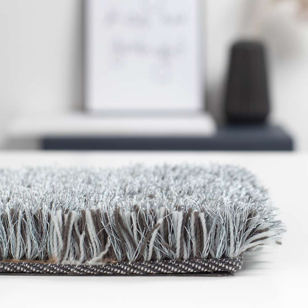 Dunkelgrauer Hochflor-Teppich Lago Mix liegt auf einem Untergrund. Der Teppich wirkt flauschig und weich, ideal für Wohnräume und bietet eine angenehme Fußwärme.