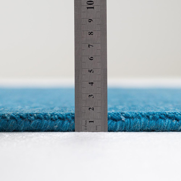 Blauer Woll-Teppich liegt flach auf einem Untergrund. Die Oberfläche zeigt eine einheitliche Textur und Farbe, die weich und gemütlich wirkt.