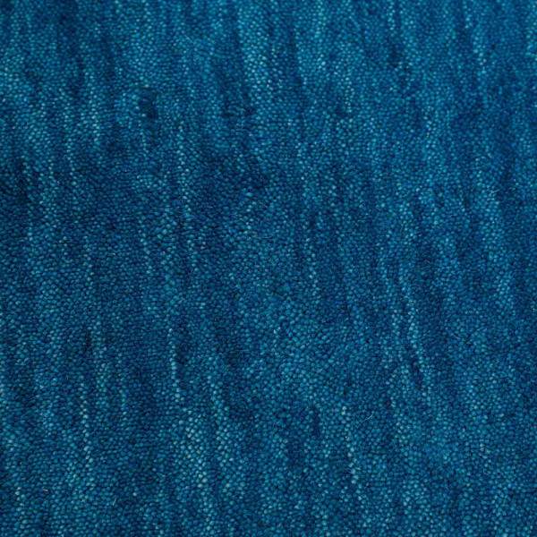 Blauer Woll-Teppich liegt flach auf einem Untergrund. Die Oberfläche zeigt eine einheitliche Textur und Farbe, die weich und gemütlich wirkt.