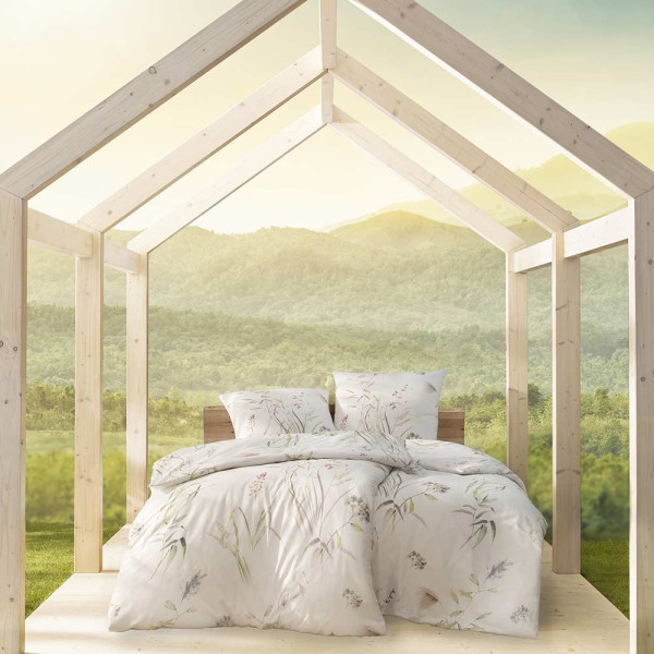 Florale Mako-Satin Bettwäsche von Estella zeigt ein Design mit zarten Pflanzenmotiven in sanften Farben. Sie liegt auf einem Bett und umfasst ein Kopfkissen und eine Decke.