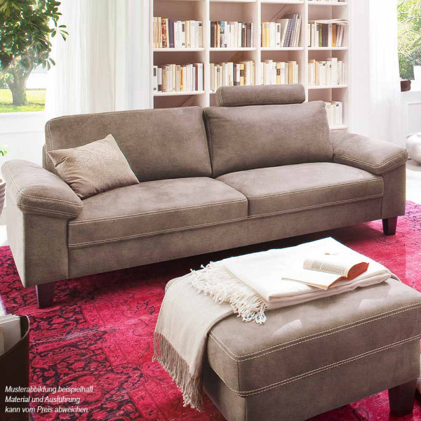 Modernes, graues 3-Sitzer-Sofa mit einer behaglichen Kissenunterlage und einer Decke auf einem roten Teppich. Im Hintergrund ist ein Bücherregal sichtbar, das mit vielen Büchern gefüllt ist.