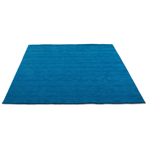 Blauer Woll-Teppich liegt flach auf einem Untergrund. Die Oberfläche zeigt eine einheitliche Textur und Farbe, die weich und gemütlich wirkt.