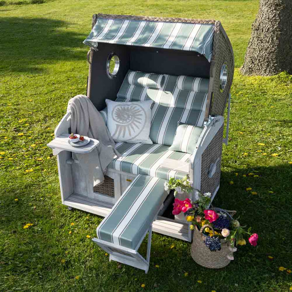 Strandkorb Fehmarn aus Pinien-Massivholz mit Rattangeflecht in grün-weiß gestreift. Er bietet gepolsterte Sitz- und Liegeflächen sowie eine Glasablage an der Seite.