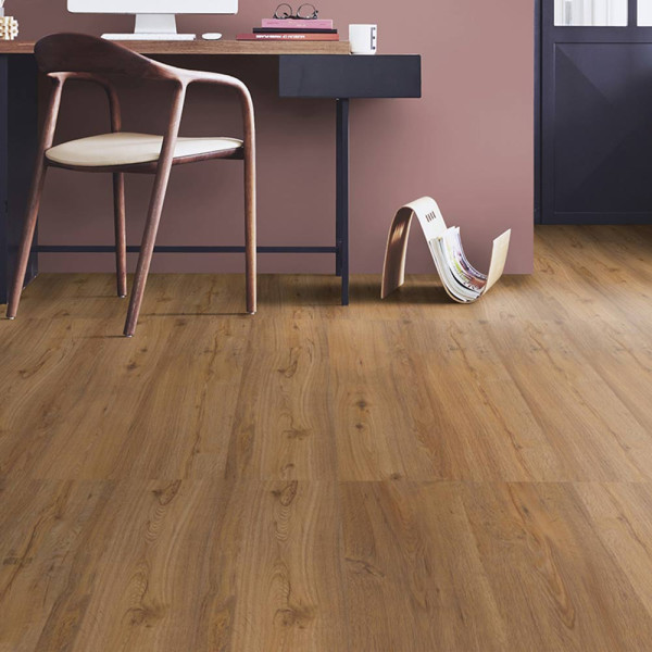 Brauner Vinylboden mit einer Holzoptik liegt in einem modernen Raum. Ein Holzstuhl steht am Schreibtisch, der eine Computertastatur und eine Tasse zeigt. An der Wand sind Zeitschriften in einem Halter angeordnet.