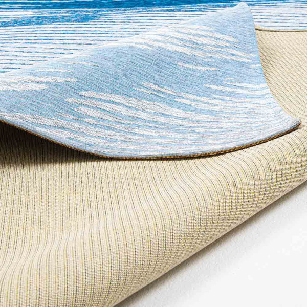 Weiß-blauer Teppich mit wellenförmigem Muster in verschiedenen Blautönen. Der Teppich hat eine flachgewebe Struktur und ist für den Innenbereich geeignet.