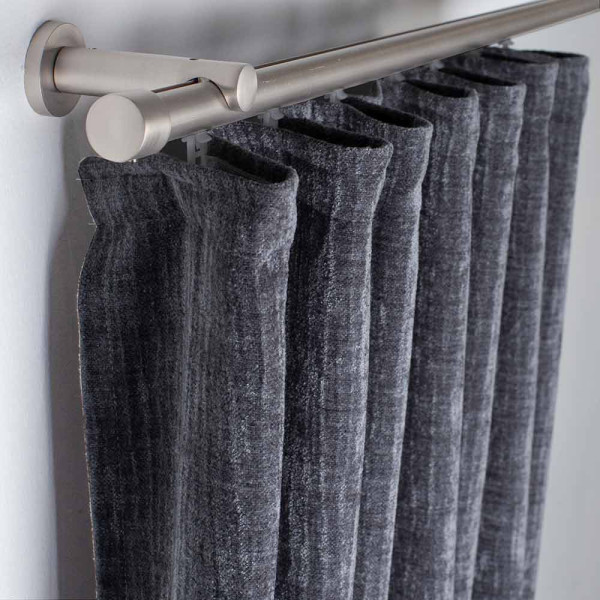 Dunkelgraue, wärmedämmende Vorhänge aus schwerem Stoff hängen an einer silbernen Gardinenstange. Die Faltenstruktur ist sichtbar, wodurch sie einen eleganten Look verleihen.