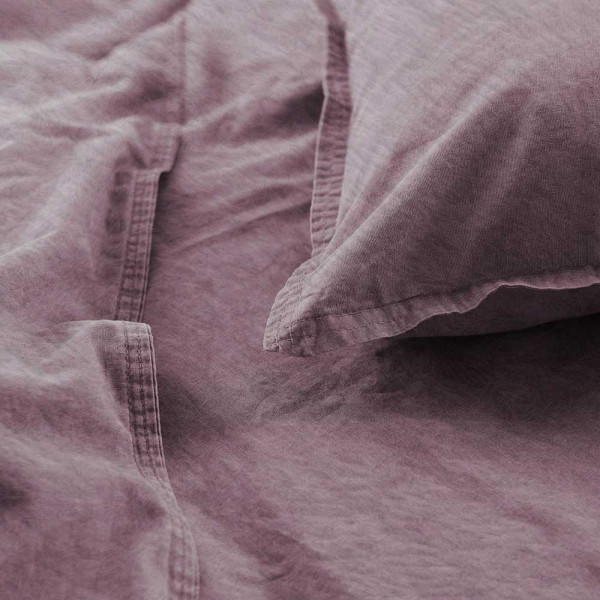 Flanell-Bettwäsche in der Farbe Mauve, bestehend aus einem Kopfkissenbezug und einem Bettdeckenbezug, liegt ordentlich auf einem Untergrund mit einer hervorgehobenen Nahtdetailansicht.
