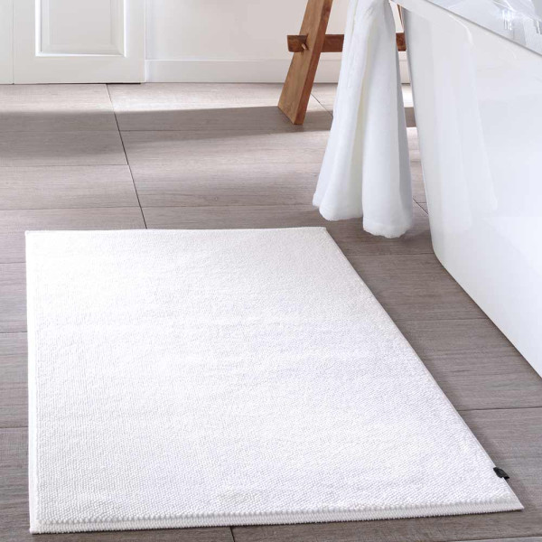 Weißer Badteppich 1007 von Cawö liegt flach auf dem Boden. Er hat eine rechtwinklige Form und eine weiche Textur. Die Maße sind 60 x 100 cm.