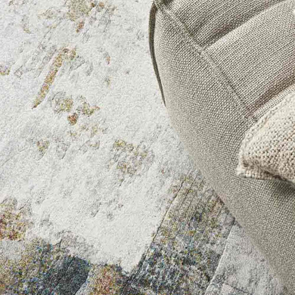 Grauer Kurzflor-Teppich Argentum 63723 mit abstraktem Muster in verschiedenen Grautönen und leicht goldfarbenen Akzenten liegt auf einem hellen Untergrund. Er vermittelt ein modernes Ambiente.