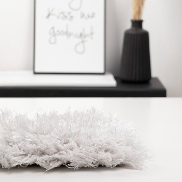 Weißer Hochflor-Teppich mit flauschiger Textur liegt auf einem Untergrund. Seine weichen Fasern verleihen dem Raum ein gemütliches Ambiente. Er ist für individuelle Maße konzipiert.