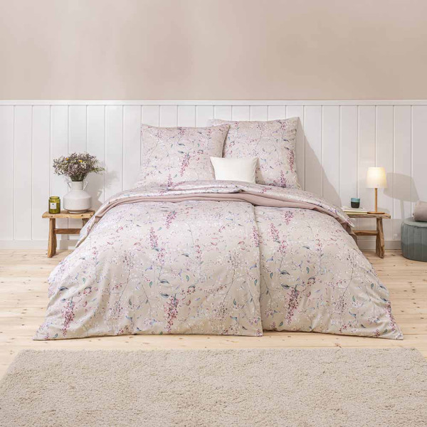 Beige Bettwäsche im floralen Design mit Blütenmustern. Die Bettdecke ist im Hintergrund sichtbar, während das Kissen im Vordergrund liegt. Ideal für eine dekorative Schlafzimmergestaltung.