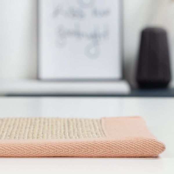 Helles Sisal-Material mit diagonalem, rosa Rand. Der Teppich zeigt eine strukturierte Oberfläche und eignet sich für individuelle Raumgestaltungen. Das nachhaltige Design betont die natürliche Materialwahl.
