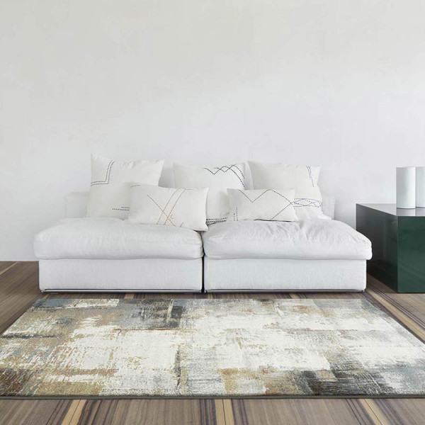 Grauer Kurzflor-Teppich Argentum 63723 mit abstraktem Muster in verschiedenen Grautönen und leicht goldfarbenen Akzenten liegt auf einem hellen Untergrund. Er vermittelt ein modernes Ambiente.