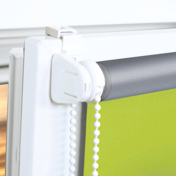 Hellgrünes Seitenzugrollo ALICIA ist im Fenster aufgewickelt und blockiert das Licht. Es wird von einer weißen Fensterleiste und einer dunklen Wand umgeben. Eine moderne Einrichtung ergänzt das Ambiente.