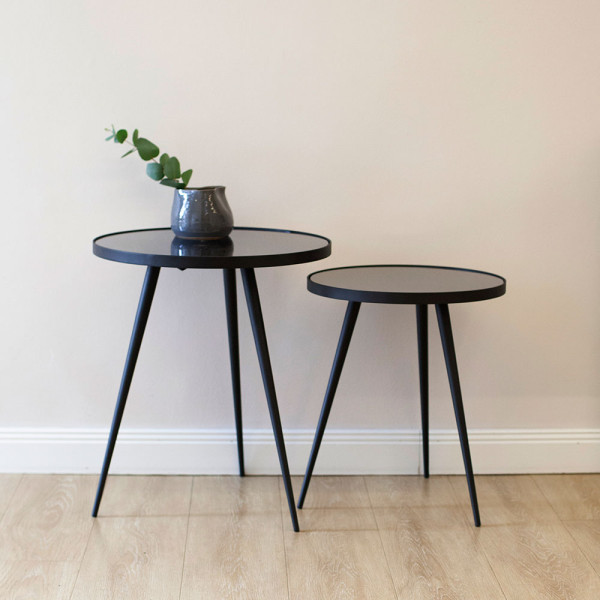 Moderner Beistelltisch mit zwei runden Glasplatten und schwarzen Beinen steht in einem minimalistischen Design. Der höhere Tisch steht über dem kleineren Tisch.