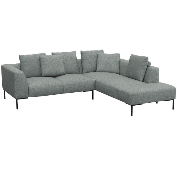 Helles, modernes Ecksofa SAVA mit offenem Ende. Das Sofa besitzt mehrere bequeme Kissen und steht auf schwarzen Metallbeinen. Es eignet sich ideal für stilvolle Wohnräume.