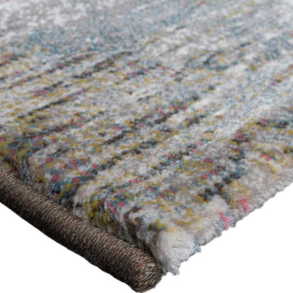 Grauer Kurzflor-Teppich Argentum 63723 mit abstraktem Muster in verschiedenen Grautönen und leicht goldfarbenen Akzenten liegt auf einem hellen Untergrund. Er vermittelt ein modernes Ambiente.