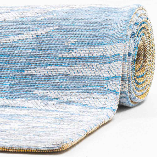 Weiß-blauer Teppich mit wellenförmigem Muster in verschiedenen Blautönen. Der Teppich hat eine flachgewebe Struktur und ist für den Innenbereich geeignet.